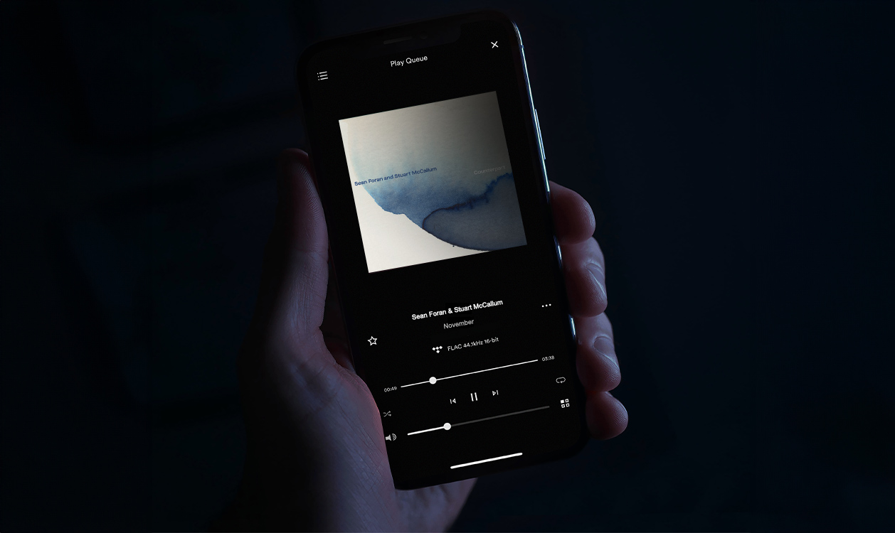 Smartphone affichant l’application Focal & Naim avec la lecture d’un album musical dans un environnement sombre.